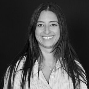 Portrait en noir et blanc d'une femme souriante aux longs cheveux bruns et portant une chemise rayée.