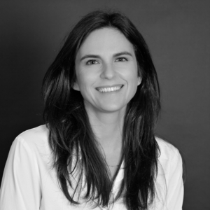 Portrait d'une femme souriante, élégante et professionnelle, en noir et blanc.