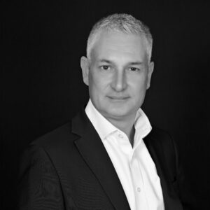 Portrait en noir et blanc d'un homme aux cheveux gris portant un costume sombre et une chemise blanche.