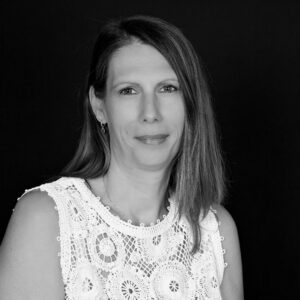 Portrait en noir et blanc d'une femme aux cheveux longs portant un haut en dentelle blanche sur fond noir.