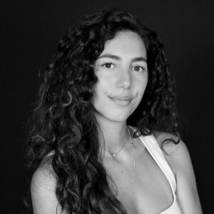 Portrait en noir et blanc d'une jeune femme aux longs cheveux bouclés et portant un débardeur blanc.